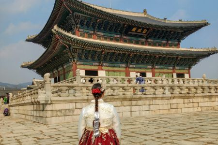 A woman dressed in hanbok looks at a palace in Seoul