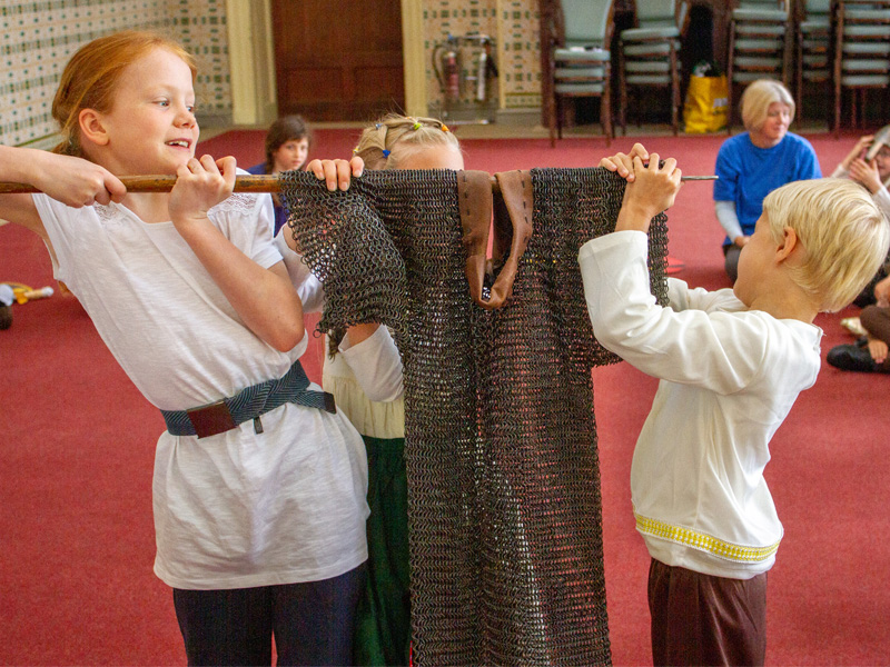 Children trying to lift some chain mail armour at a Marvellous History Workshop